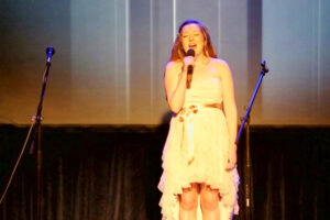 A woman in white dress singing on stage.