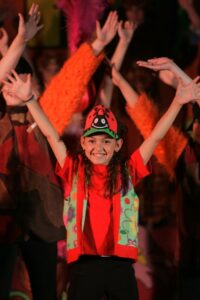 A girl in red shirt and hat with hands up.