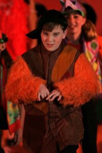 A boy in costume and orange fur on stage.