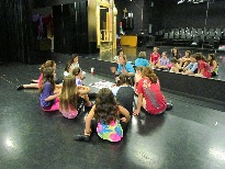 A group of children sitting on the floor in front of a stage.
