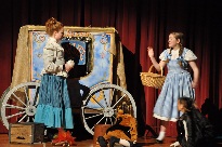 Two girls in costume on stage with a wagon.